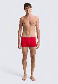 Punased puuvillased bokserid, mis istuvad tihedalt, ees tasku, sile vöökoht, nähtavaid mustreid ega logosid pole.