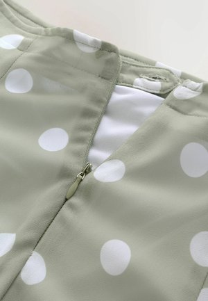 Material verde deschis cu buline mari albe, prevăzut cu închidere cu fermoar la spate și textură netedă. Design cu mâneci scurte.