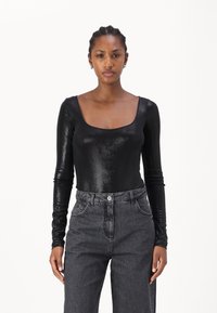 Body nero a maniche lunghe realizzato in un materiale lucido con scollatura quadrata, abbinato a jeans scuri grigi a vita alta.