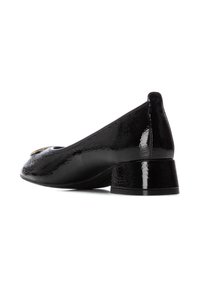 Zapato de charol negro con punta redonda, pequeño tacón de bloque y acento dorado en la punta. Textura lisa y brillante, diseño minimalista.