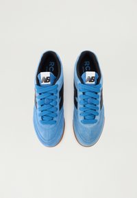 Baskets en daim bleu avec des rayures noires sur les côtés, forme à bout rond et lacets texturés. Présentent une étiquette blanche sur la languette et une semelle en caoutchouc.