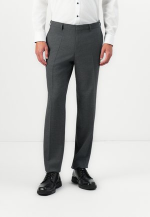Man wearing gray dress pants, black dress shoes, and a white buttoned shirt standing against a white background.