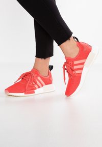 Červené textilní sportovní boty s třemi bílými pruhy, šněrovací design a černý opatek; gumová podrážka s polstrovanou mezipodrážkou.