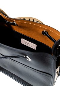 Interno di una borsa a tracolla in pelle nera, con fodera in tessuto beige, etichetta con il marchio Coccinelle, hardware argentato e chiusure a cordoncino arrotondate.