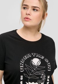Zwart katoen t-shirt met een witte grafische print van een blad en een bloemontwerp met de tekst "UNDER THE SUN" in een cirkelvormige lay-out.
