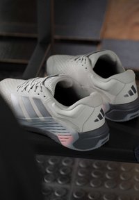 Двойка светлосиви атлетични обувки Adidas с черно лого на петата, поставени върху тъмен фон с плочкиран под.