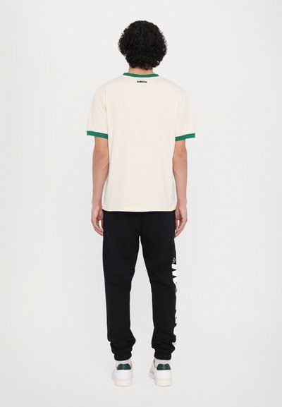 Cream short-sleeve t-shirt with green ribbed collar and cuffs, worn with black joggers featuring a white logo print on the leg.