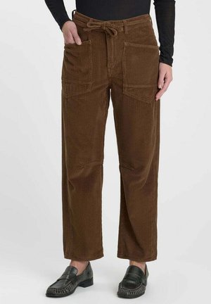 Pantaloni marroni in velluto a coste con tasche applicate frontali e vita annodata, indossati con mocassini neri e top nero a maniche lunghe.