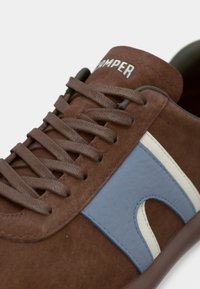 Καφέ δερμάτινο αθλητικό παπούτσι από σουέντ με μπλε και λευκές λεπτομέρειες, διαθέτει επίπεδα κορδόνια και στρογγυλεμένη μύτη. Λογότυπο "Camper" στη γλώσσα.