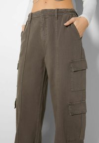 Pantalones cargo en un verde oliva apagado, con una cinturilla elástica, bolsillos laterales y múltiples bolsillos cargo en ambas piernas. Tejido de algodón.
