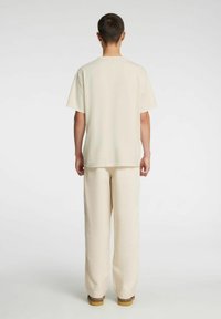 Koszulka o luźnym kroju w kremowym kolorze oraz pasujące szerokie spodnie, wykonane z miękkiego materiału, o prostym wzornictwie bez widocznych wzorów ani logo.