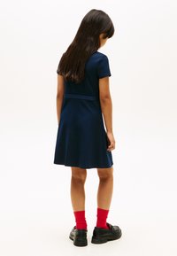 Σκούρο μπλε φόρεμα με κοντά μανίκια, φαρδύ φόρεμα και λεπτομέρεια στη μέση. Συνδυασμένο με κόκκινες κάλτσες και μαύρα παπούτσια. Απλό, λείο ύφασμα.