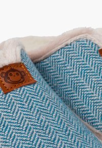 Błękitne kapcie w wzór jodełki z miękkim różowym wnętrzem oraz brązową skórzaną metką z wzorem małpki. Materiał wydaje się puchaty i ciepły.