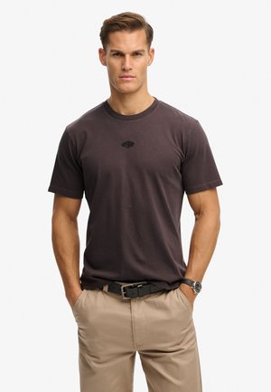 T-shirt corto grigio scuro con scollo rotondo e un piccolo logo sul petto, abbinato a pantaloni beige e una cintura nera.