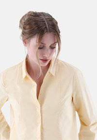 Yellow shirt made of smooth fabric, featuring a button-up front, collar, and a tailored fit with vertical seam details on the sides.