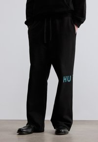 Μαύρη φόρμα από απαλό ύφασμα με ελαστική μέση, με τυρκουάζ λογότυπο "HU" στο αριστερό πόδι. Φαρδιά εφαρμογή, ίσια κοπή.