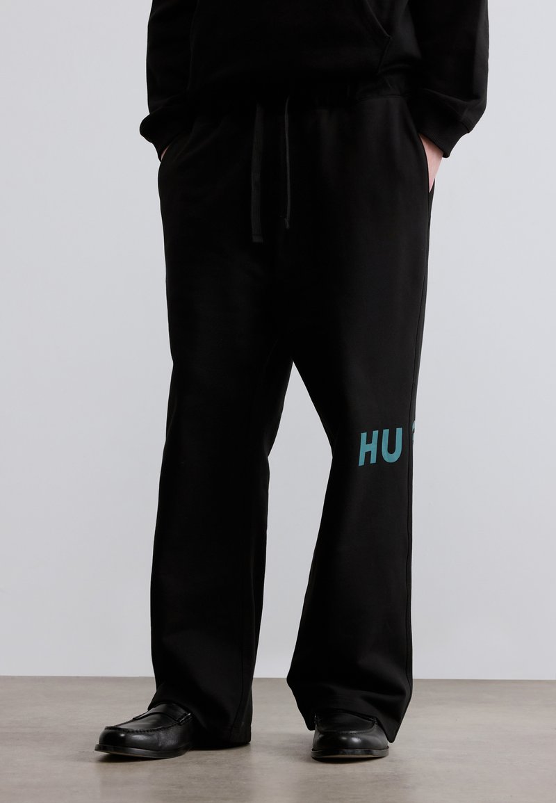 Μαύρη φόρμα από απαλό ύφασμα με ελαστική μέση, με τυρκουάζ λογότυπο "HU" στο αριστερό πόδι. Φαρδιά εφαρμογή, ίσια κοπή.