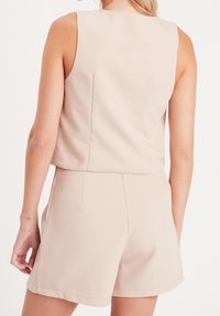 Beige mouwloze top gecombineerd met bijpassende shorts. De stof lijkt glad, heeft een getailleerde pasvorm en beschikt over minimale stiksels en zakken.
