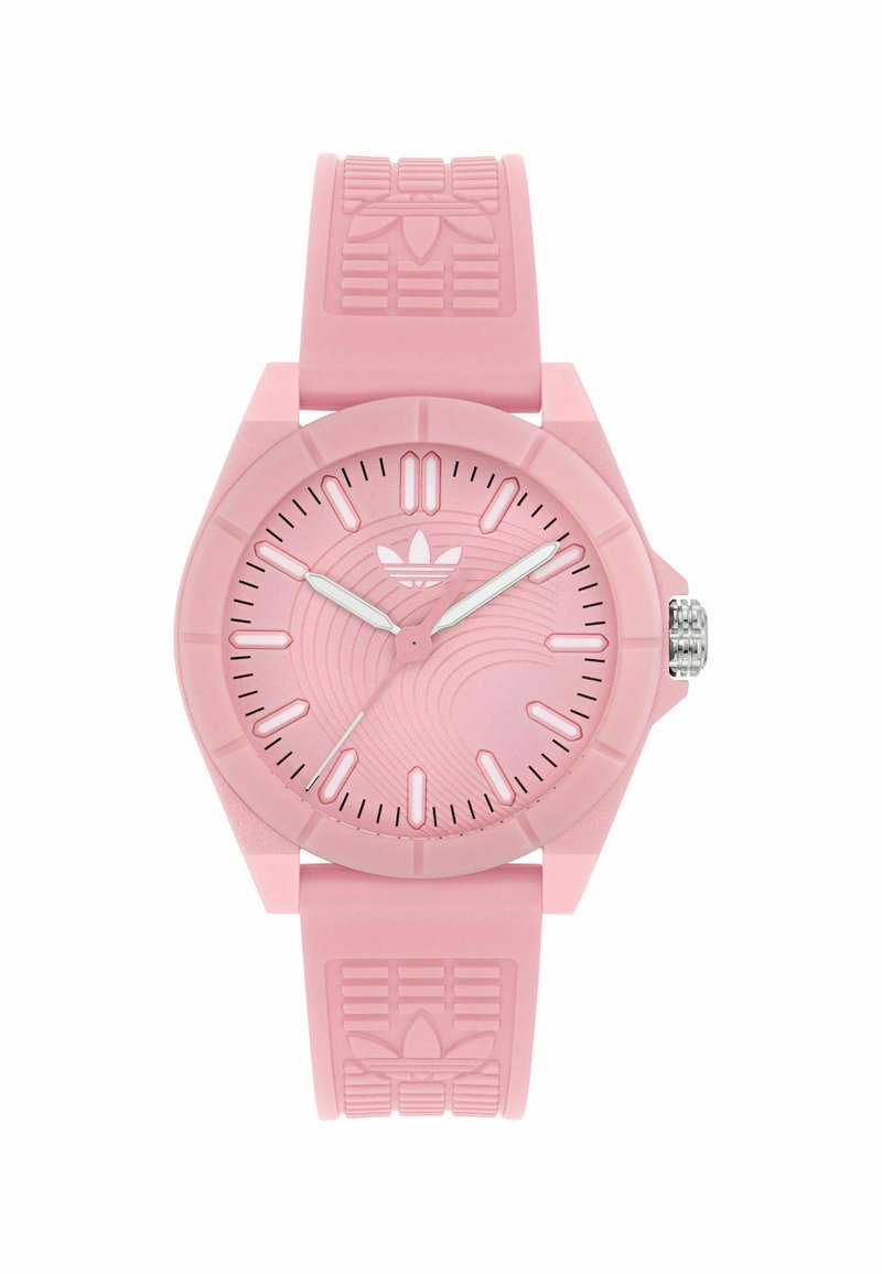 Montre en silicone rose avec un cadran rond, un bracelet texturé et des aiguilles argentées. Présente un motif de vagues sur le cadran et le logo Adidas sur le bracelet.