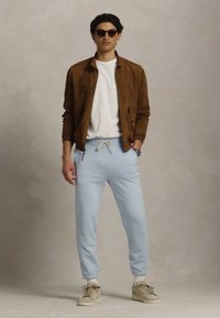 Ανοιχτό μπλε φόρμες με μανσέτες, λευκό μπλουζάκι και καφέ σουέτ μπόμπερ τζάκετ. Καφέ αθλητικά παπούτσια και σκούρα ηλιακά γυαλιά ολοκληρώνουν την εμφάνιση.