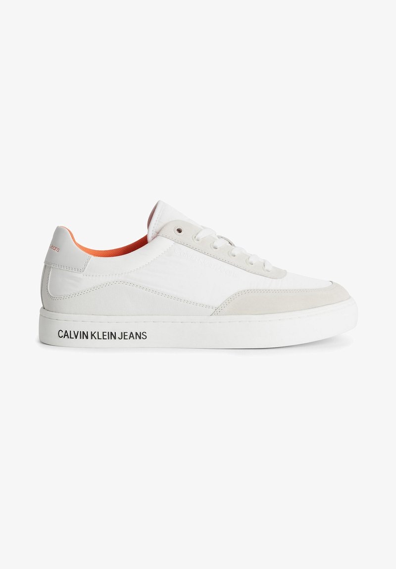 White athletic sneaker with gray suede accents, textured fabric panels, patterned sole, and orange interior. Features "CALVIN KLEIN JEANS" logo.