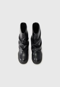Bottines noires en cuir avec un design froncé, texture lisse, bout arrondi et semelle en caoutchouc texturé.