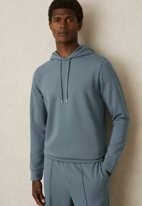 Felpa con cappuccio in blu tenue, realizzata in tessuto morbido. Presenta un cappuccio con coulisse, maniche lunghe e una vestibilità rilassata. Fa parte di un completo coordinato.