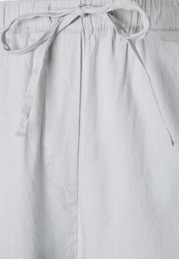 Shorts en tissu gris clair avec taille à cordon, dotés d'une poche avant et d'une texture douce. Design simple, adapté pour une tenue décontractée.