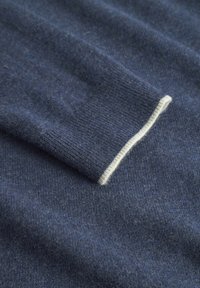 Tessuto a maglia blu navy con una consistenza morbida. Presenta un bordo a contrasto di color crema lungo il bordo dei polsini.
