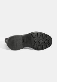Zwarte rubberen schoenzool met een gestructureerd oppervlak en geribbelde profiel voor grip. Heeft een gladde en matte afwerking.