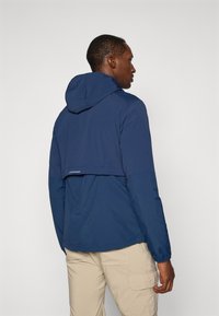 Marineblå letvægtsjakke med hætte, har en cropped bagdesign, elastiske manchetter og en subtil refleksdetalje.