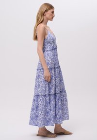 Robe maxi à motif floral bleu clair. Caractéristiques : bretelles fines, couches superposées et taille cintrée. Tissu léger et fluide.