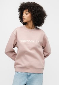 Ροζ φούτερ με λαιμόκοψη crew, ριμπ μανσέτες και άνετη εφαρμογή. Διαθέτει λευκό λογότυπο "carhartt" στην μπροστινή πλευρά. Συνδυάζεται με ανοιχτόχρωμα τζιν παντελόνια.