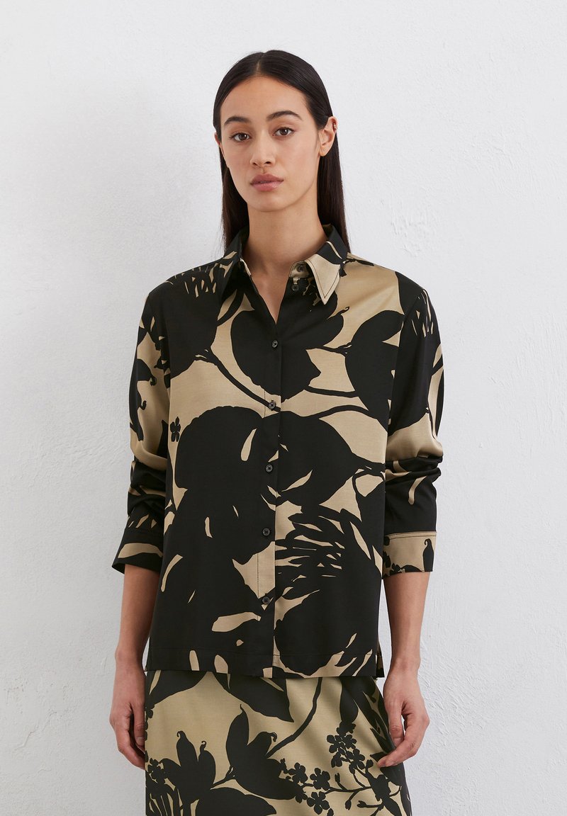 Chemise à manches longues avec imprimé floral noir et beige, col pointu et texture subtile. S'associe avec une jupe assortie.