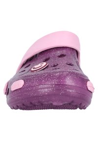 Lila Clogs mit einem rosa Riemen, mit einem gesprenkelten Design und Belüftungslöchern. Ein kreisförmiges Logo ist auf der Seite sichtbar. Weiches Material.