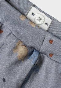 Grauer Stoff mit einer weichen Textur, versehen mit gedruckten Tiermotiven und kleinen Blumenmustern. Mit einem weißen Knopf in der Taille geschlossen.