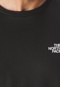 Schwarzes Baumwoll-T-Shirt mit Rundhalsausschnitt, auf der oberen linken Seite mit einem kleinen weißen Logotext "THE NORTH FACE". Glatte Textur.