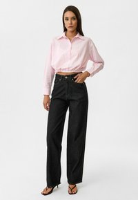 Lichtroze cropped shirt met knoopsluiting, gecombineerd met zwarte high-waisted wijde broek met een klassiek vijf-pocket ontwerp.