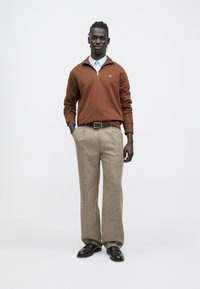 Barna cipzáras pulóver világoskék galléros inggel, bézs texturált nadrággal és sötét cipővel párosítva. Egyszerű, tiszta dizájn.