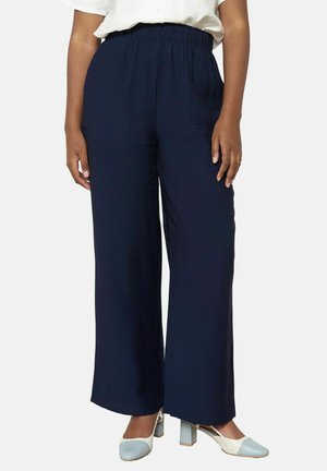 Pantalones de pierna ancha color navy con una cinturilla elástica, fabricados con un material suave. Combinados con zapatos de tacón bloque en azul claro y blanco.