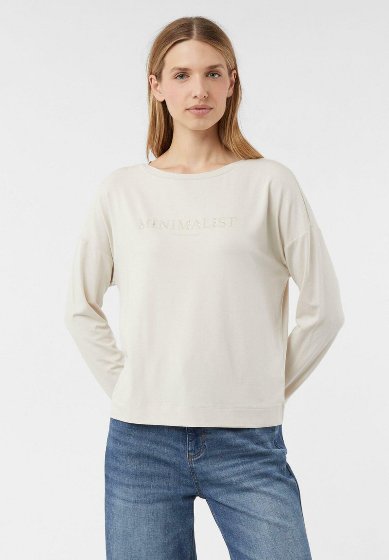 Béžová košile s dlouhým rukávem a kulatým výstřihem, s nápisem "MINIMALIST" v jemném, reflexním materiálu. Měkká látka s volným střihem.