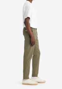 Pantalons chinos verts olive à coupe droite, en coton, avec des détails cousus et des poches, associés à un t-shirt blanc basique et des baskets.