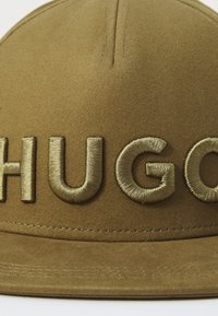 Barna sapka nagy, hímzett "HUGO" felirattal, amely megegyező árnyalatú. Az anyaga sima, struktúrált formával és lapos karimával rendelkezik.