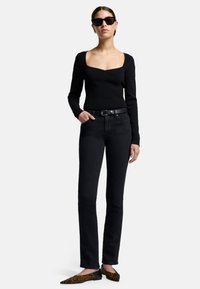 Schwarzes, geripptes Langarm-Oberteil mit quadratischem Ausschnitt, kombiniert mit schwarzen geraden Jeans und Ballerinas im Leopardenmuster. Accessoires sind schwarze Sonnenbrillen.