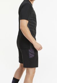 Svart sporttröja med strukturerade horisontella ränder, kombinerad med svarta shorts med en lila mönstrad ficka. Mjukt tyg och figursydd design.