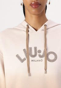 Kapućasta majica u gradijentnoj breskvastoj nijansi, sa logom od rhinestona "LIU JO MILANO" i beoškim vezicama sa metalnim završecima.