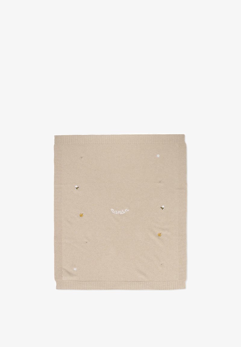 Coperta in maglia beige con bordi a coste, decorata con api ricamate, una foglia e stelle, con la parola "nanán" in un carattere bianco curvo.