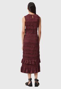 Abito midi bordeaux con texture arricciata, design senza maniche, dettaglio con apertura a chiave sul retro e orlo arricciato. Realizzato in un tessuto morbido con finitura liscia.