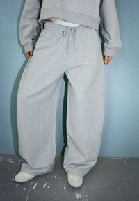 Gray wide-leg sweatpants with elastic waistband and drawstring. Smooth fabric with a soft texture, complemented by light-colored footwear.