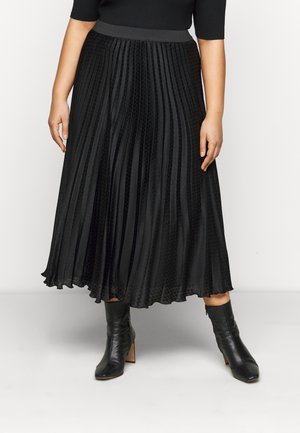 Falda negra plisada con un tejido texturizado, que presenta una cintura suave, una silueta fluida y un dobladillo en capas. Combinada con botines negros hasta el tobillo.